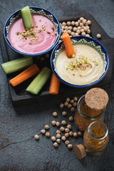 Black wooden serving board with hummus, carrot and cucumber slices, studio shot on a dark-grey stone background
