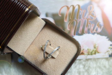 Couple rings placed in an open box and  background  is a blurred photos about cake at the wedding of  the newlyweds. 