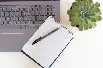 Office desk with laptop, notepad and succulent cactus on a white table