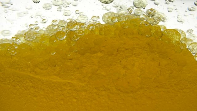 Close shot of golden liquid on a white background. Close-up view of bio fuel shot in a research laboratory. Golden background of poured sesame oil and black cumin oil, resulting in bubbles and bulbs.