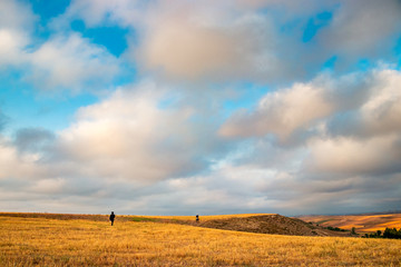 two adventurers walking in amazing endless fields with beautiful blue sky and lovely white clouds above their head and enjoying the freedom and peace.