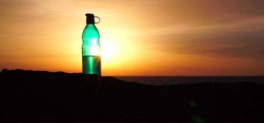 Reusable glass water bottle on the sea coast at sunrise. Zero Waste Lifestyle