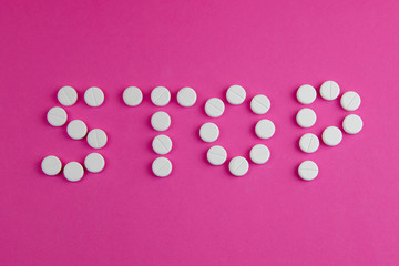 The word stop is made of tablets on a pink background. Top views