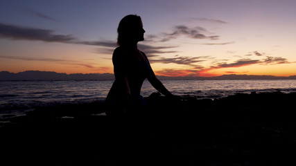 Silhouette woman meditates against the sea at colorful sunset.