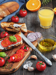 Fresh sandwiches baguette , tomatoes, vegetables and olive oil, ingredients for making a vegan sandwich, close-up. Freshly squeezed citrus juice in a glass. Dark rustic wooden background.