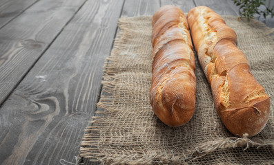 Two fresh french baguettes made from white flour cools after baking. Bread located on burlap, rustic dark wooden background. Close-up, copy space for text. Horizontal layout