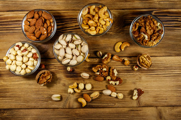 Assortment of nuts on wooden table. Almond, hazelnut, pistachio, walnut and cashew in glass bowls. Top view. Healthy eating concept