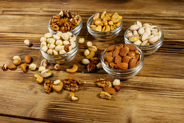 Assortment of nuts on wooden table. Almond, hazelnut, pistachio, walnut and cashew in glass bowls. Healthy eating concept