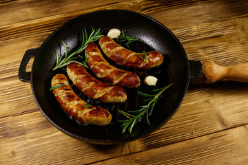 Fried sausages with rosemary, garlic and spices in cast iron grill frying pan on wooden table