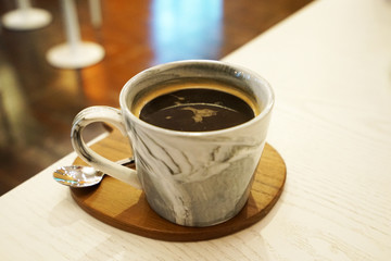 Close up ceramic porcelain cup of hot black Americano coffee on wooden tray table
