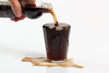 Human hand pouring cola from plastic bottle into overflowing glass with ice cubes. Isolated on...