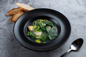 Cod ear soup with fresh spinach and cod pieces on stone background