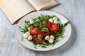 Classic italian caprese with ripe tomatoes, mozzarella cheese, basil and pesto sauce. Shot in a rustic style on wooden table with a vintage book.