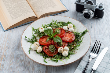 Classic italian caprese with ripe tomatoes, mozzarella cheese, basil and pesto sauce. Shot in a rustic style on wooden table with a vintage book.