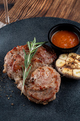 Juicy pork neck steak with chilli sauce and grilled half of garlic, served on black plate