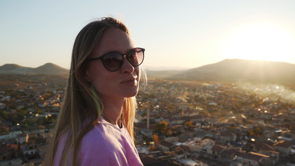 Young caucasian blonde female standing over ancient city and looking in camera