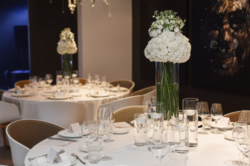 round served table with tablecloth with plates, glass, fork . festive table in restaurant decorated fresh flowers on birthday on wedding party. banquet table for guests in stylish cafe interior 