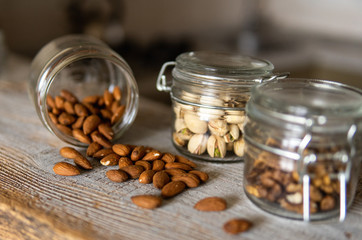 Almonds scattered on the white vintage table from a jar and with other nuts on background. Almond is a healthy vegetarian protein nutritious food. Almonds on rustic old wood.