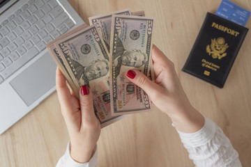 woman hold banknote 50 U.S. dollars in hand and count it. American passport with boarding pass and laptop on the table. Travel concept. Cash. Flat lay