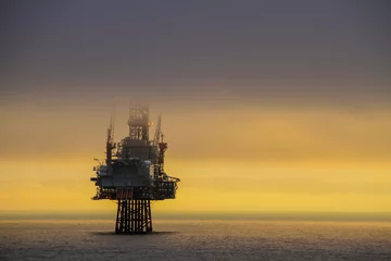 Selbstklebende Fototapeten NORTH SEA, NORWAY - 2011 APRIL 15. Oil platform Ringhorn in the North Sea with low clouds cover the drilling tower with beautiful sunset in the background © Arild