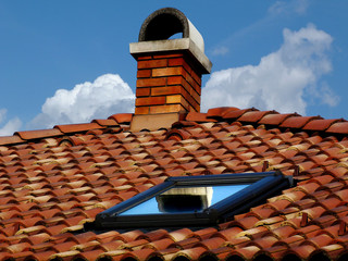 Naklejka premium sloped terracotta clay roof ridge closeup detail. bright textured clay roofing. glass skylight. blue sky. fluffy white clouds. bright sunlight. construction industry and residential building materials