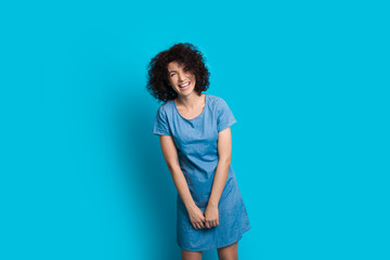 Curly haired caucasian woman posing in a nice dress on a blue background while smiling cheerfully