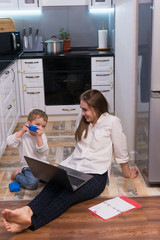 Family, mother working on laptop with child. Beautiful business mom is using computer and spending...