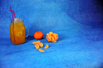 Glass mug of citrus juice with ice with slices of mandarin on a blue background. © Алексей Желтухин