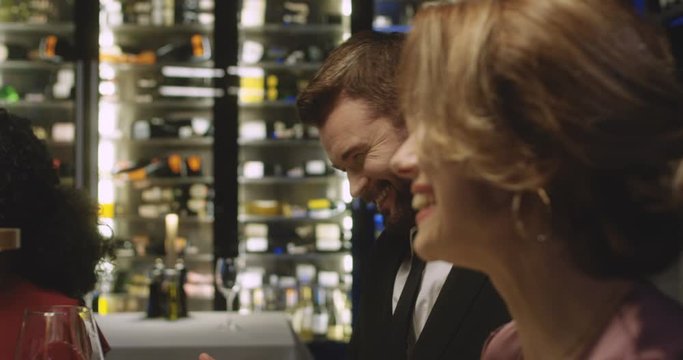 Close up of joyful multiethnic two couples laughing while sitting at table in restaurant. Caucasian and African American men and women talking and joking at dinner while clasing with glasses of wine.