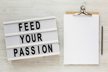 'Feed your passion' words on a modern board, clipboard with blank sheet of paper on a white wooden background, top view. Overhead, from above, flat lay.