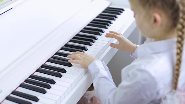 Little girl plays classical music on a white piano