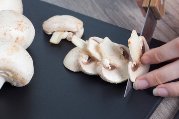 Pieces of champignon mushrooms. The girl cuts the mushrooms into even pieces with a knife. Cooking by a female chef. Top view on a black cutting Board. Food, vegan, vegetarian, dietary.