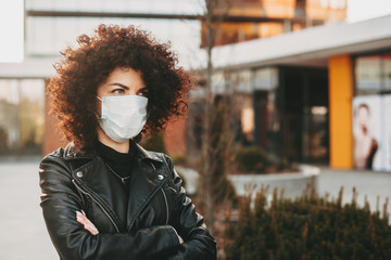 Caucasian lady with curly hair is posing with crossed hands while wearing an anti virus mask