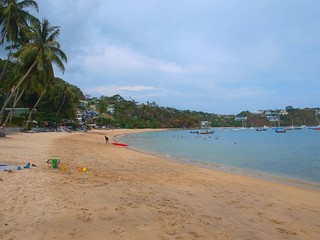 A beach on a tropical island with people resting on it, a man drags from a sea a red canoe on the sand. Family beach vacation at a tropical resort.