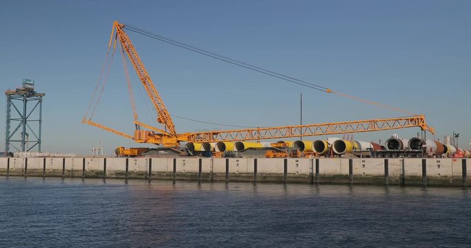 ROTTERDAM, THE NETHERLANDS - CIRCA 2019: Storage and loading site for elements of wind turbines to be assembled for huge off-shore wind farms under construction on the North Sea. Huge metal tubes.