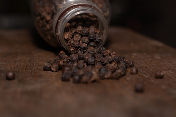 A pepper seed spilled out of a close-up jar with a wooden board background.