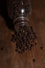 A pepper seed spilled out of a close-up jar with a wooden board background.