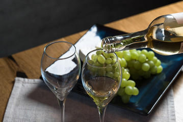 Pouring white wine from bottle into the wineglass on the table