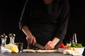 Chef cook slicing olives. Against the background of vegetables. Cooking, tasty and wholesome food.