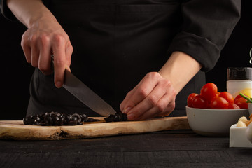 Chef cook slicing olives. Against the background of vegetables. Cooking, tasty and wholesome food.