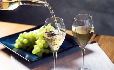 Pouring white wine from bottle into the wineglass on the table