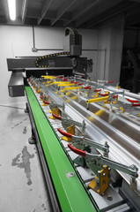 CNC machine with a metal panel clamped onto the bed in a factory workshop.  With selective colour