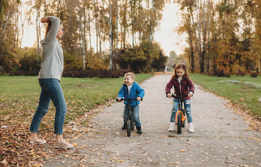 Fototapeta premium Caucasian mother giving the start for her kids who are riding the bikes in a sunny autumn day