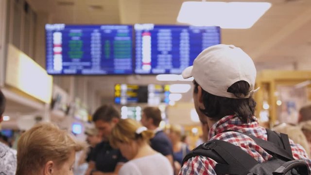 Backpacker checking flight information on digital schedule display inside arrival hall in international airport.