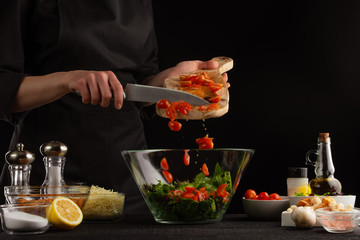 Chef cooks a salad with spinach leaves, sprinkles cherry tomatoes. Freezing in motion. On a black...