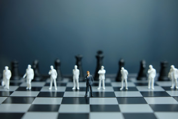 Business strategy conceptual photo -  Painted miniature of businessman standing in front of unpainted people and chess pieces on a chessboard that forms a barrier