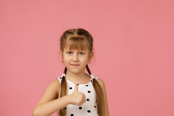 happy beautiful little child girl in dress showing thumbs up on pink background.