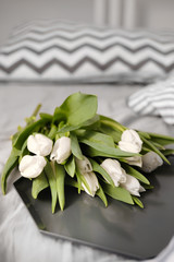 Bouquet of beautiful white tulips on the bed in the interior in a Scandinavian style. 