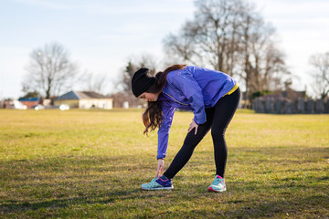 Obraz premium A young Caucasian woman in sports clothes is engaged in warm-up and fitness in the Park, doing bends to the leg. The concept of sport, health and active life