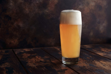 A large mug of golden beer stands on a wooden background in a bar